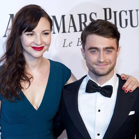 Erin Darke und Daniel Radcliffe posieren zusammen auf einem roten Teppich. Sie strahlen in die Kameras und umarmen sich gegense…
